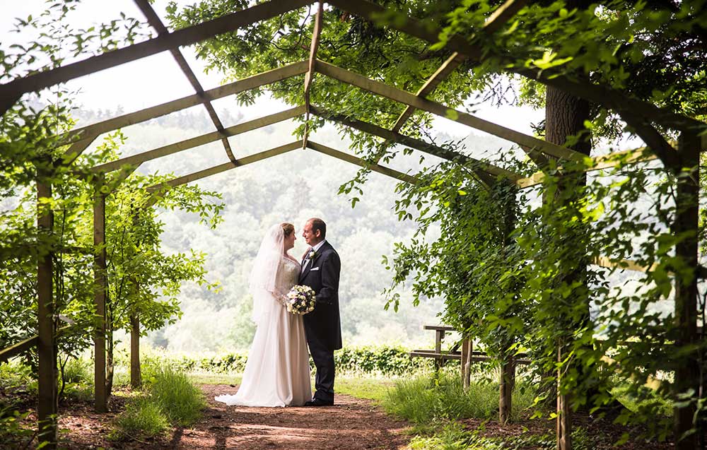 Bride and groom under laburnum arch at Arley Arboretum